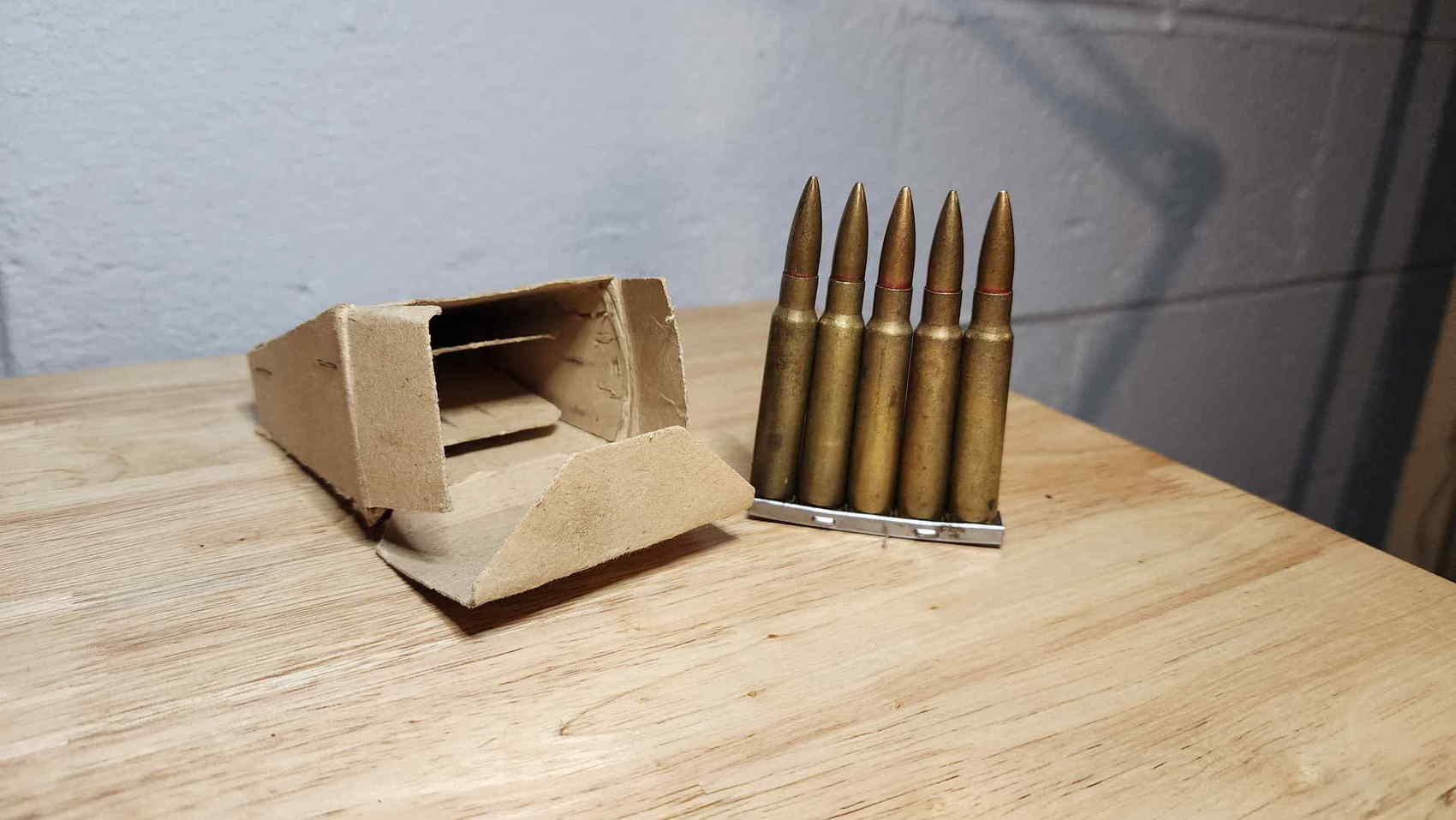Five Type 99 cartridges on a steel clip beside a cardboard ammunition box