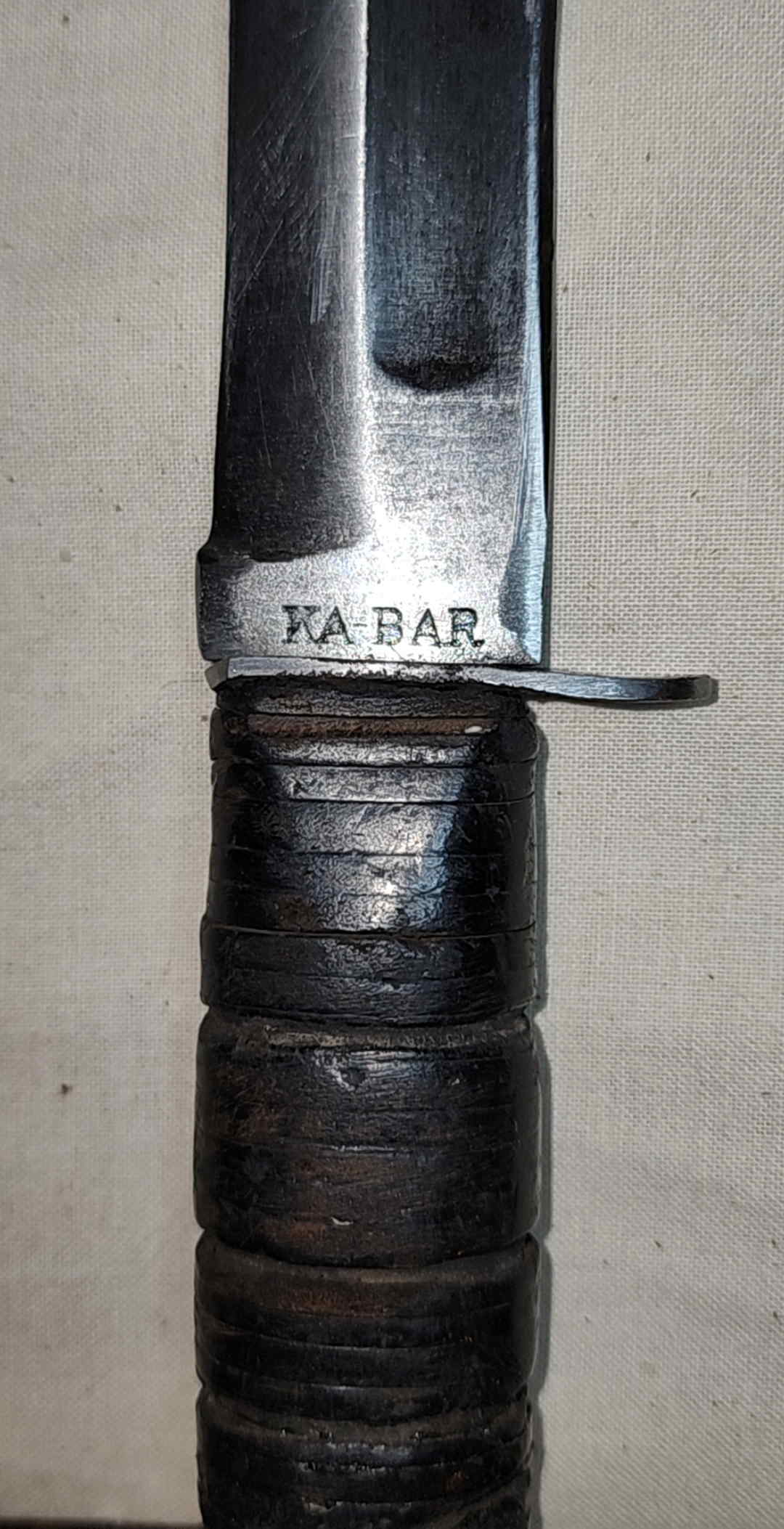 Close view of the KA-BAR blade marking and shortened steel crossguard